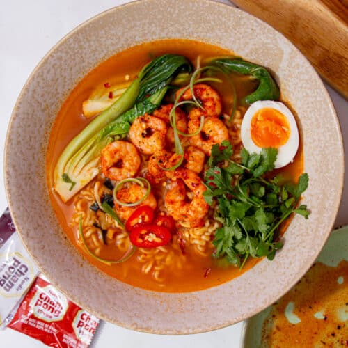 A bowl of ramend with golden browned shrimp, pak choi and topped with an egg and coriander in a bowl.