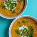Red lentil soup in 2 white bowls and topped with yogurt and parsley
