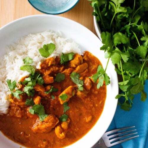 Chicken tikka in a white bowl with rice and topped with coriander