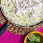Risotto cooked in frying pan and topped with white fish and garnished with limes