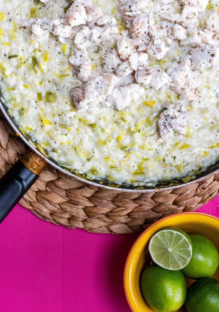 Risotto cooked in frying pan and topped with white fish and garnished with limes