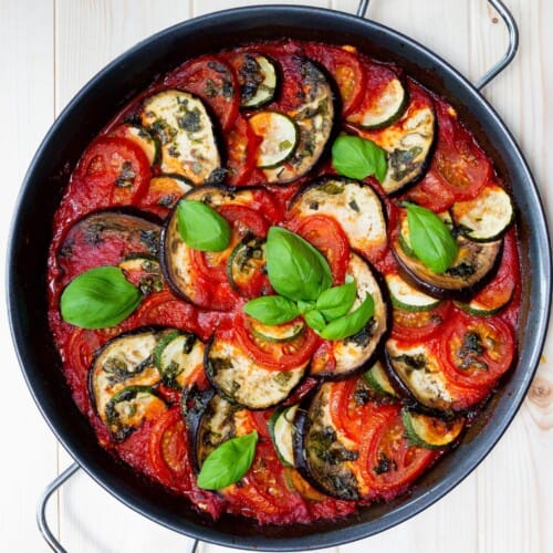 Ratatouille in a metal pan with 2 handles and garnished with basil