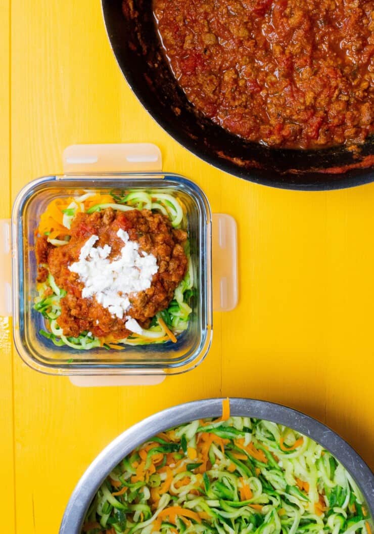 Bolognese sauce in metal wok and glass meal prep container filled with vegetables and bolognese sauce