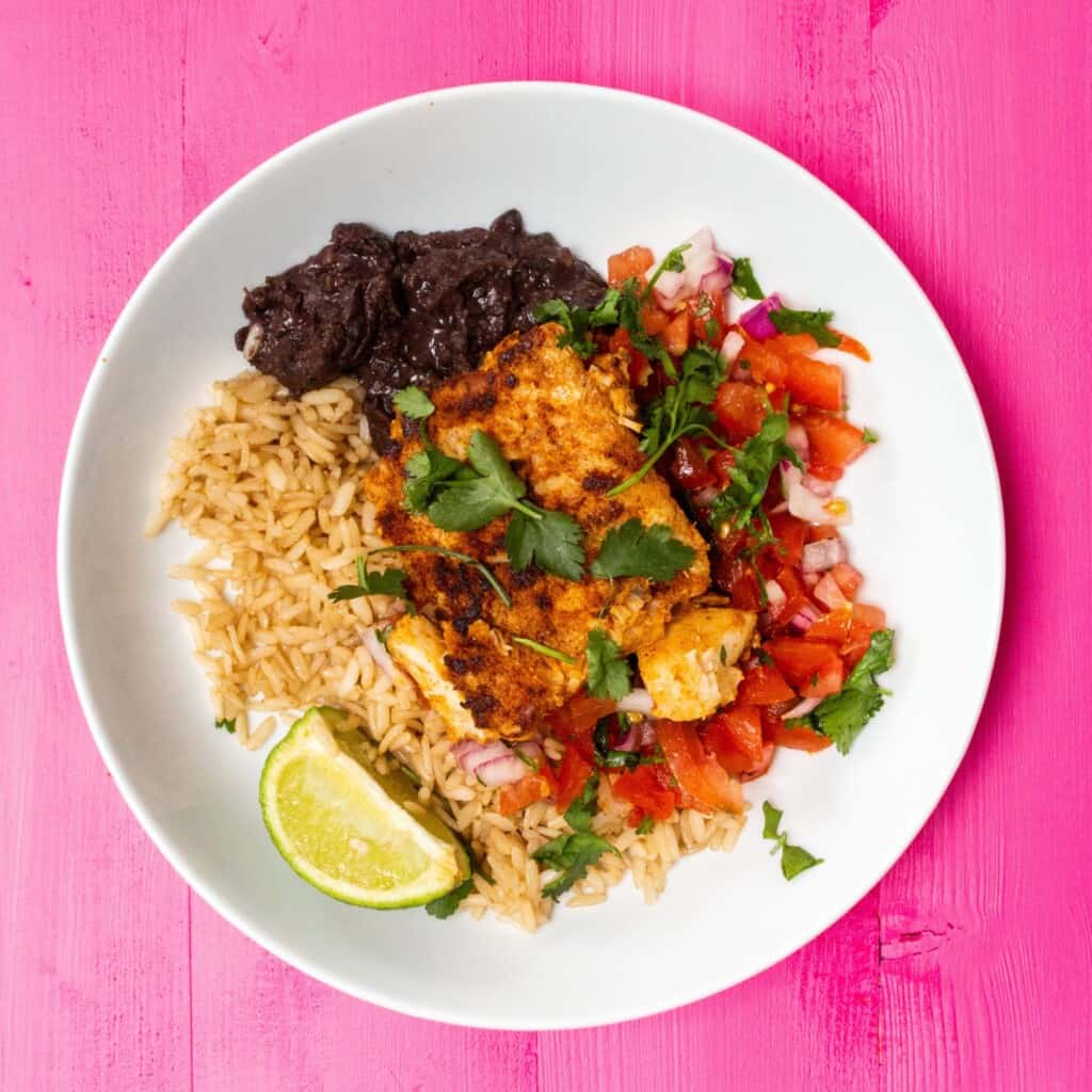 A bowl of fish, with chopped tomatoes, black beans, brown rice and a wedge of lemon