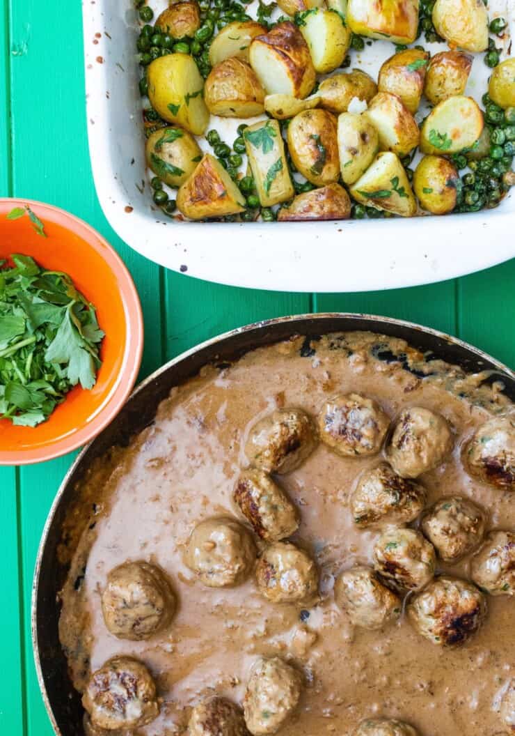 A large pan of meatballs in gravy with a dish of roasted new potatoes