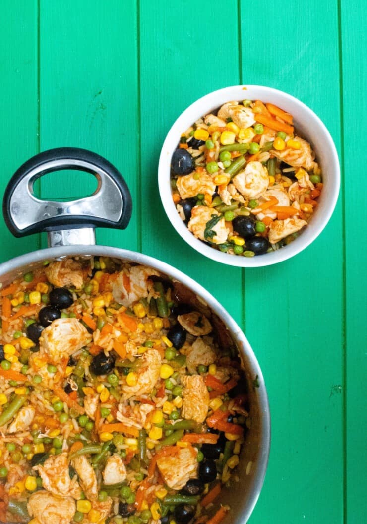 Overhead shot of large frying pan with yellow rice mixed with vegetables and olives