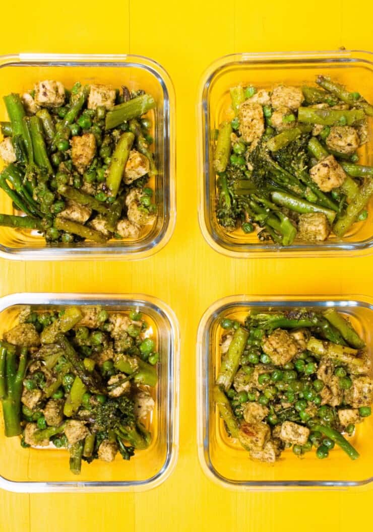 Overhead shot of 4 glass meal prep containers filled with cubes of cooked quorn with pesto and vegetables