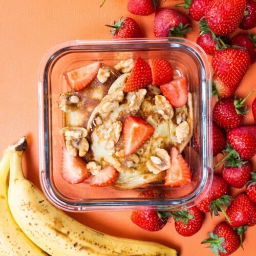 Overhead shot of glass meal prep container with banana pancakes topped with strawberries
