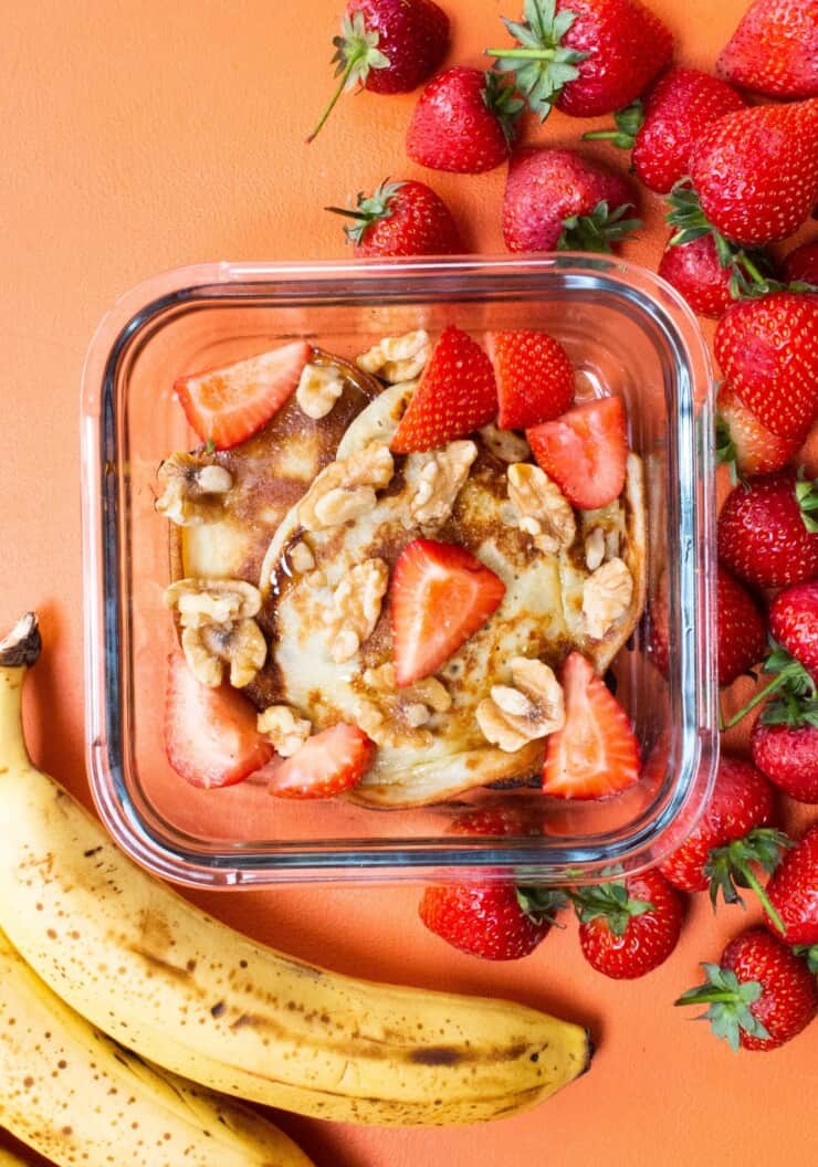 Overhead shot of glass meal prep container with banana pancakes topped with strawberries