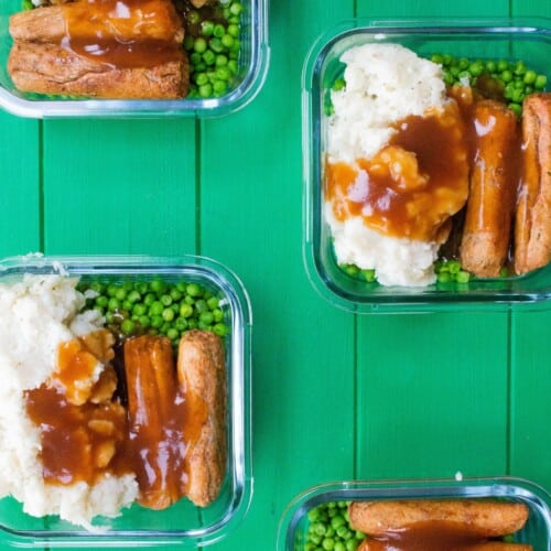 Overhead shot of veggie sausages and mash with peas and gravy in glass meal prep containers