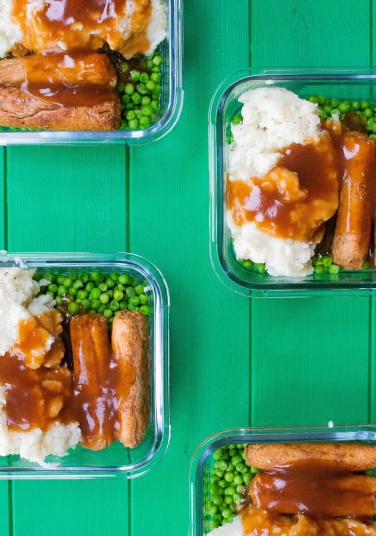 Overhead shot of veggie sausages and mash with peas and gravy in glass meal prep containers