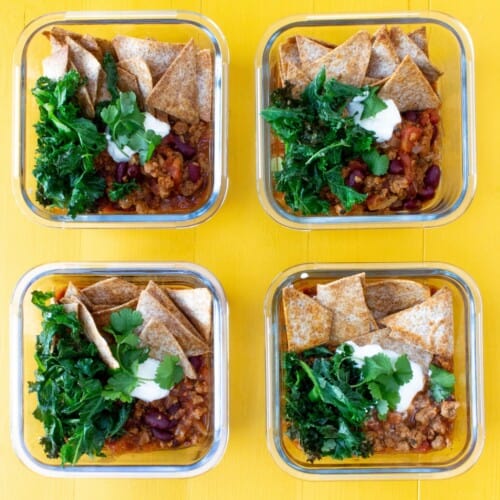 Overhead shot of 4 glass meal prep containers loaded with vegetarian mince, kale and nachos