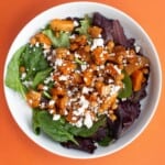 Roasted butternut squash, chickpea, spinach and feta salad on a white bowl on an orange background.