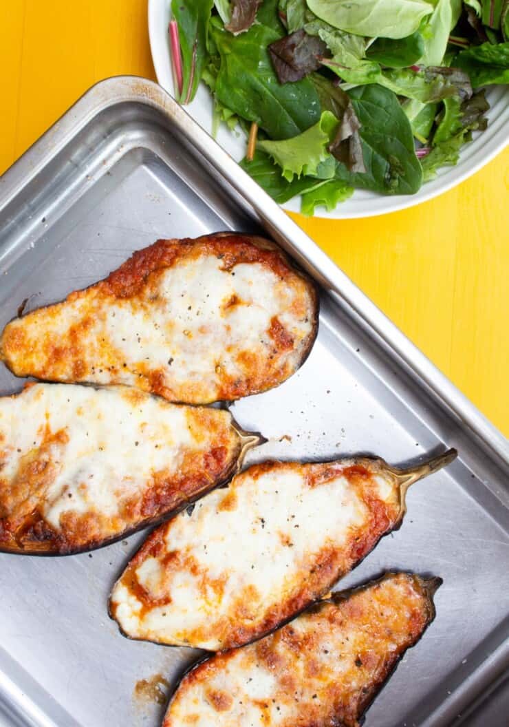 Overhead shot of 4 aubergine halves topped with melted cheese on stainless steel baking tray