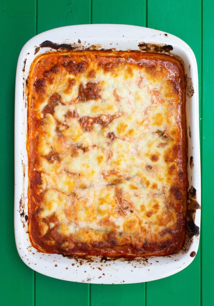 Overhead shot of cooked lasagna in white baking dish on green background