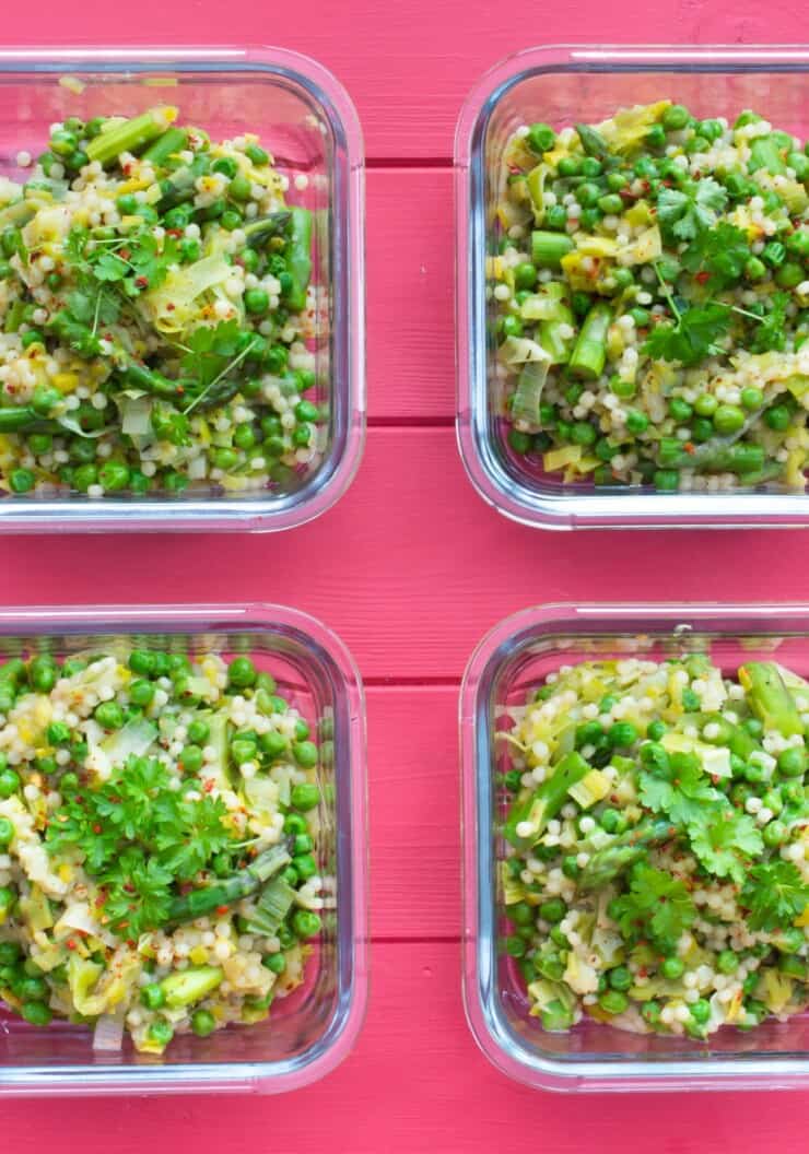 Overhead shot of 4 glass meal prep containers filled with giant cous cous and greens