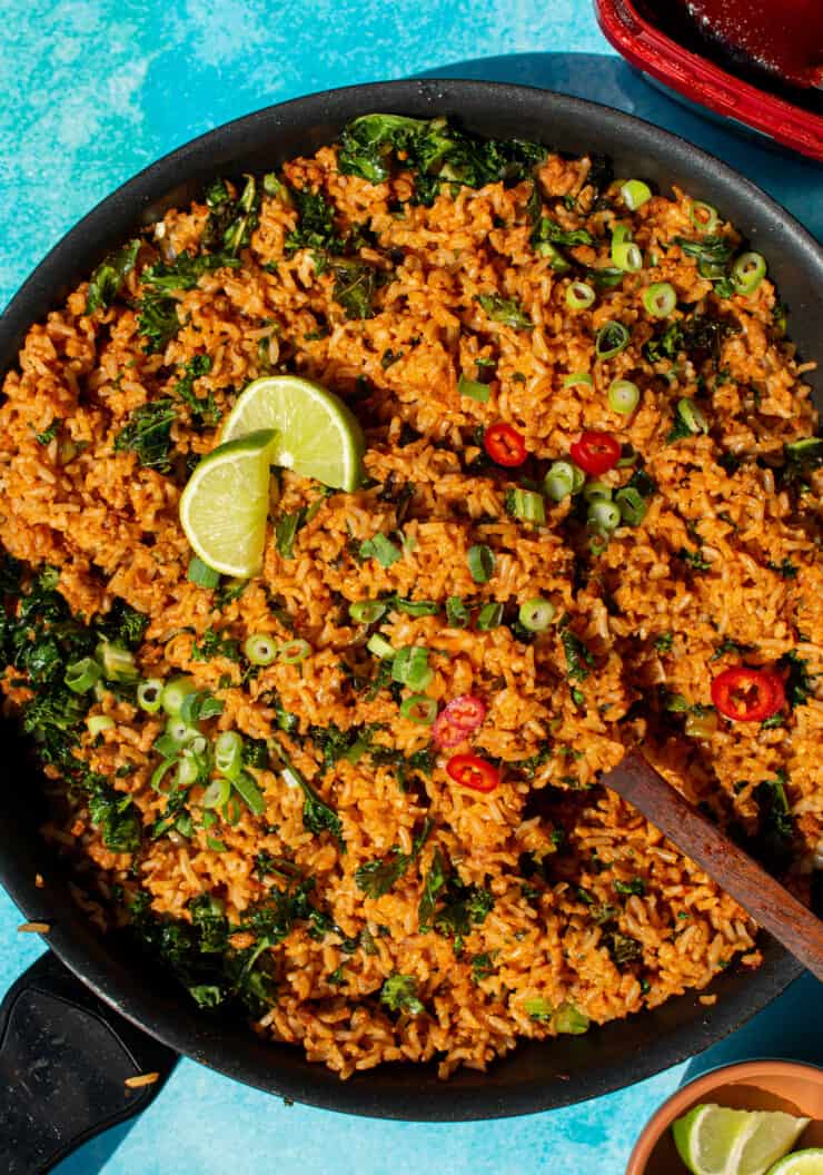 Turkey Mince Recipe with Gochujang Fried Rice with kale topped with slices of spring onion and lime wedges in a large pan on a blue background.