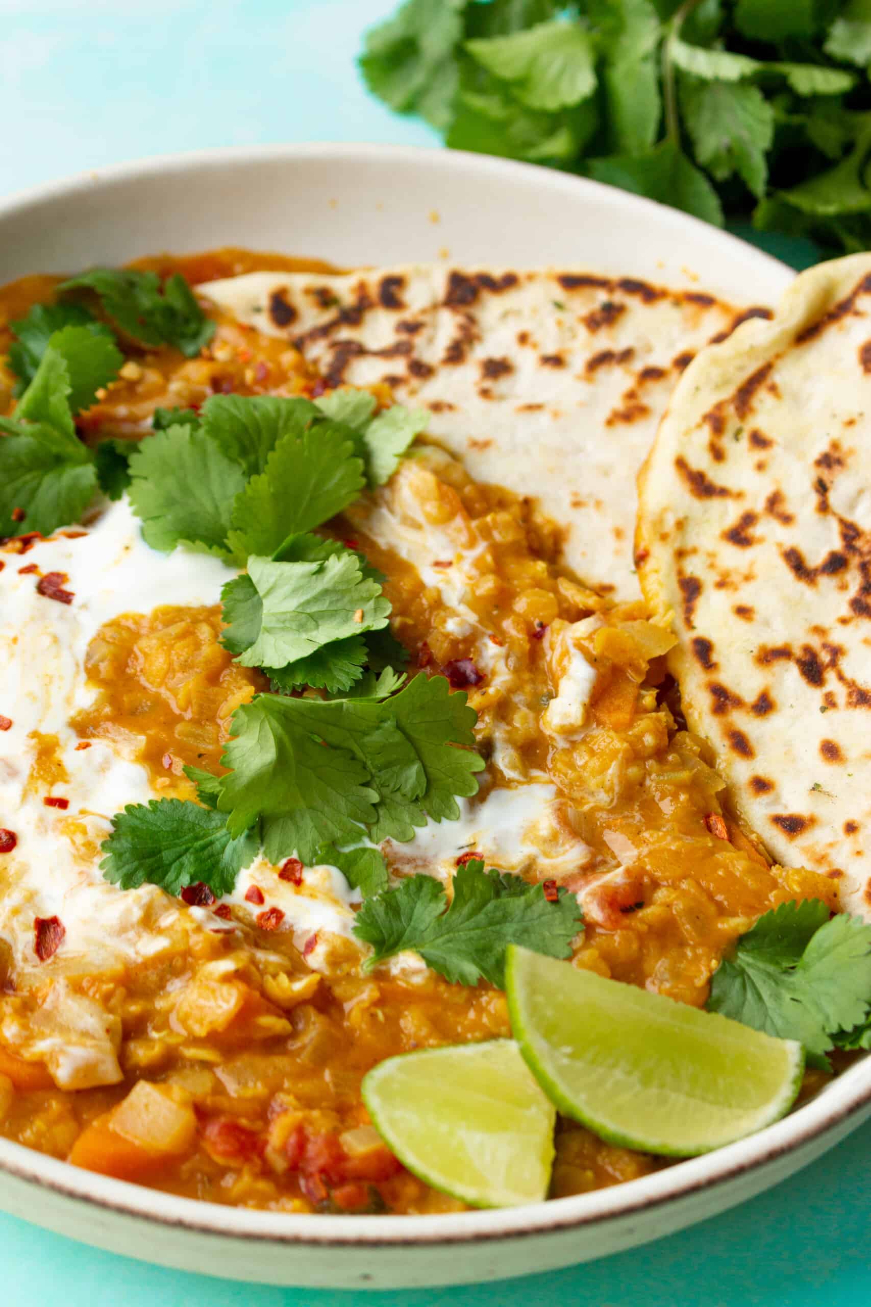 Red lentil dahl topped with coriander, lime wedges, chilli flakes and naan bread.