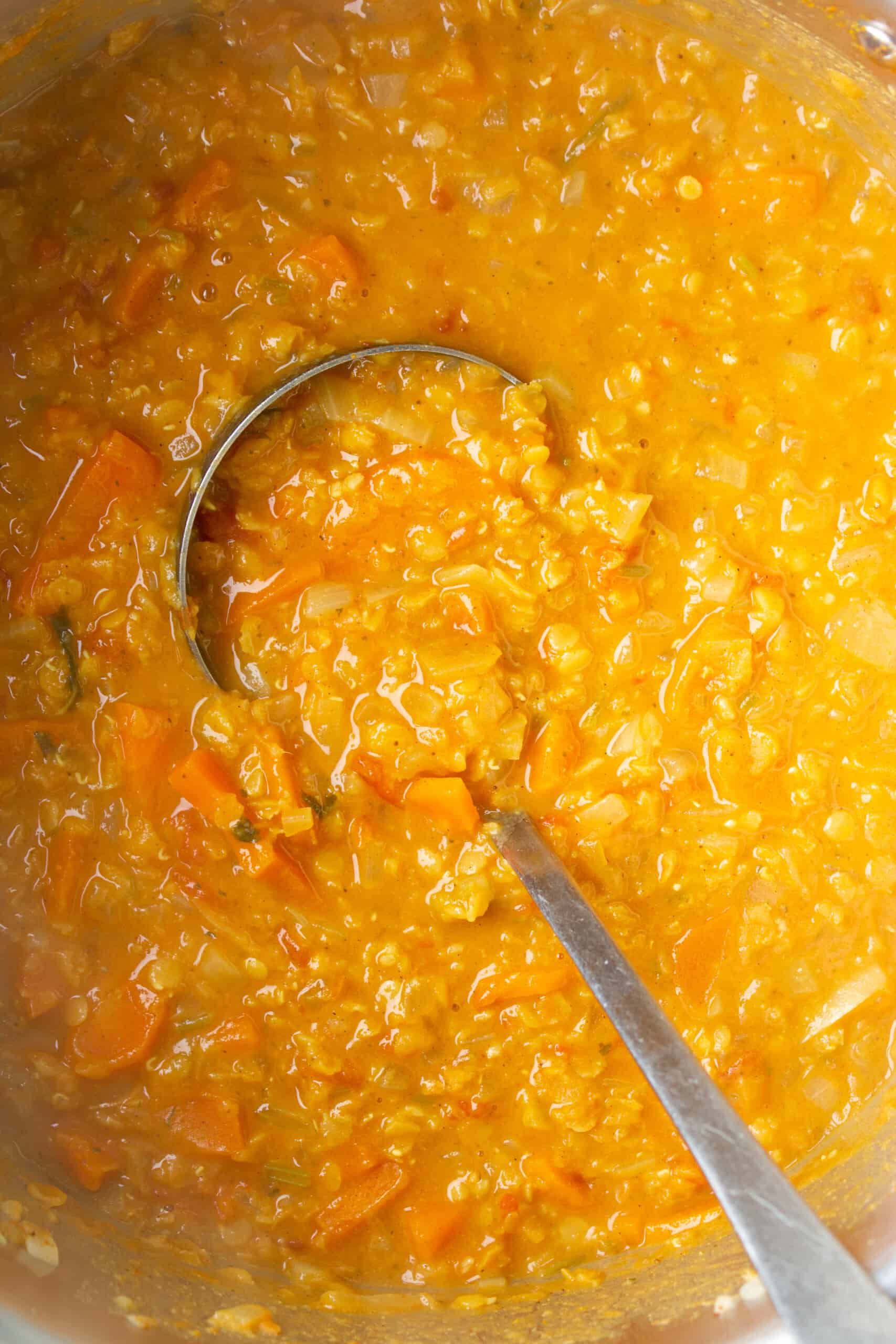 Close up of red lentil dahl with a metal ladle in pan.