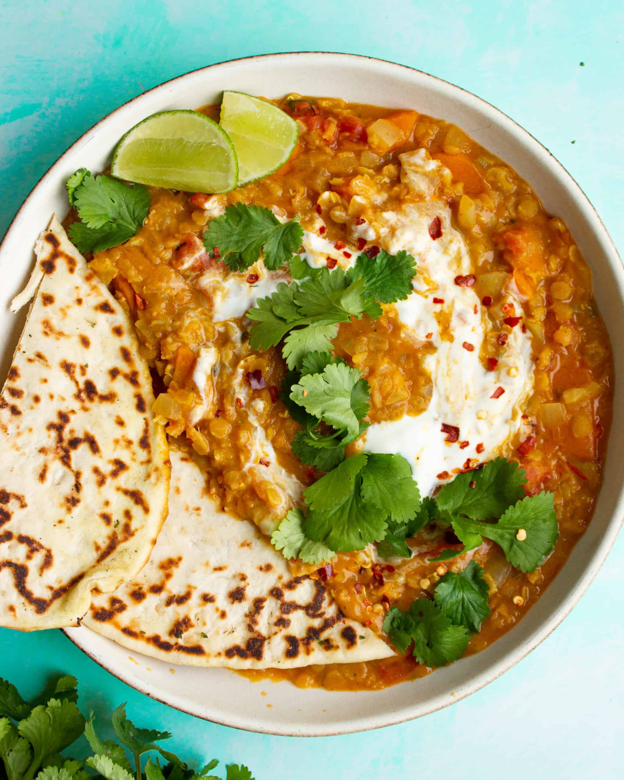 Overhead shot of red lentil dahl with naan bread, lime wedges and coriander 