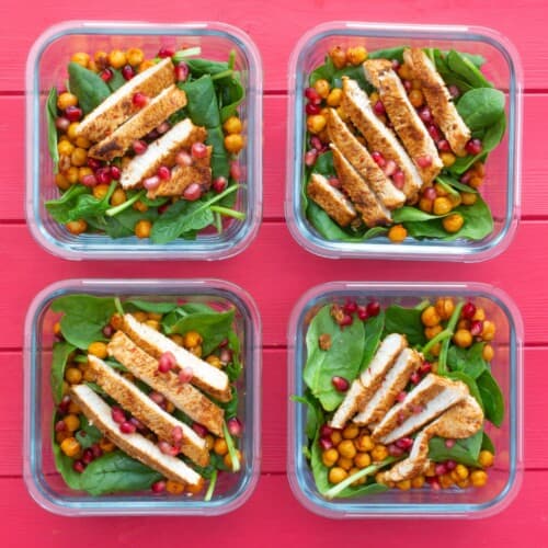 Overhead shot of 4 glass meal prep containers filled with spinach, turkey slices and roasted chickpeas