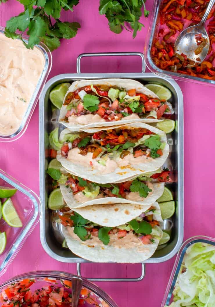 Overhead shot of tacos in a metal tray with fillings in operate containers