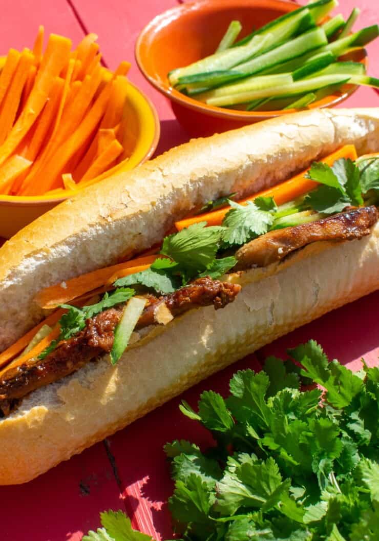 Side shot of large baguette filled with pork, carrot stick and salad