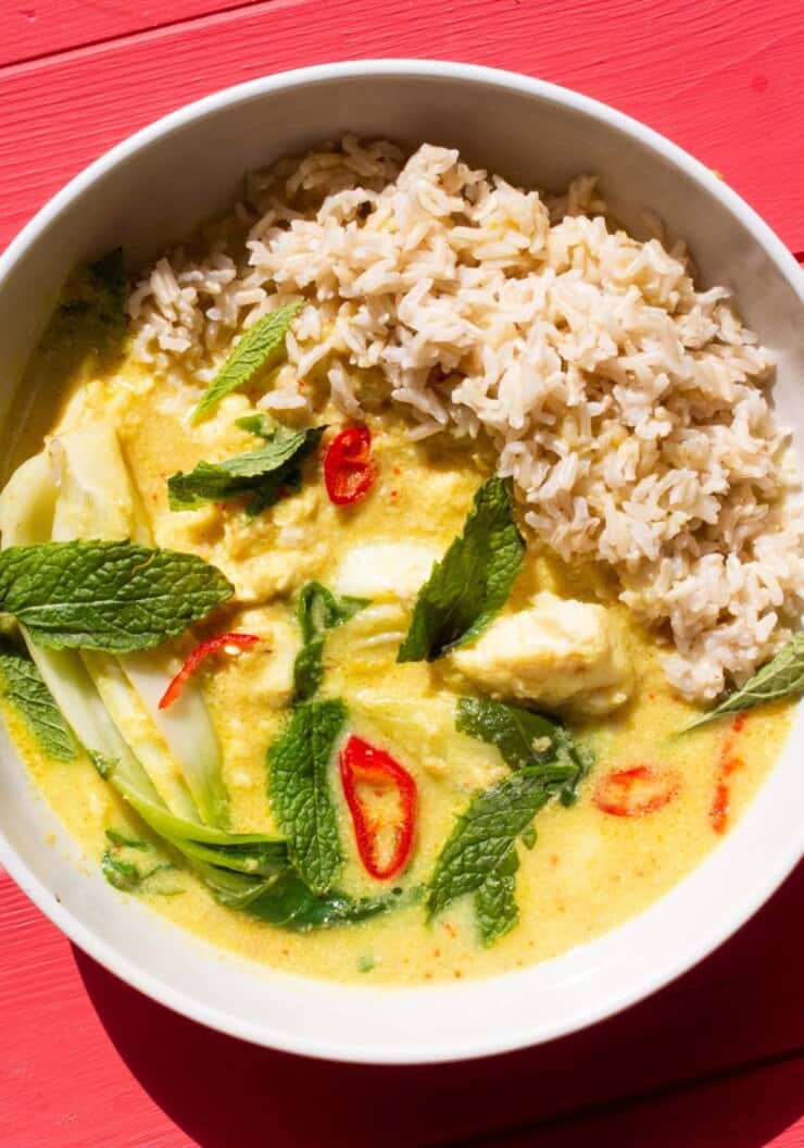 Overhead shot of a bowl of fish amok curry with rice and topped with mint leaves