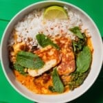 Overhead shot of curry with rice, browned halloumi slices, mint and a slice lime