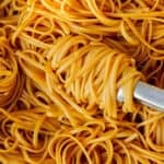 Close up of cooked spaghetti being stirred with some tongs with a sauce.