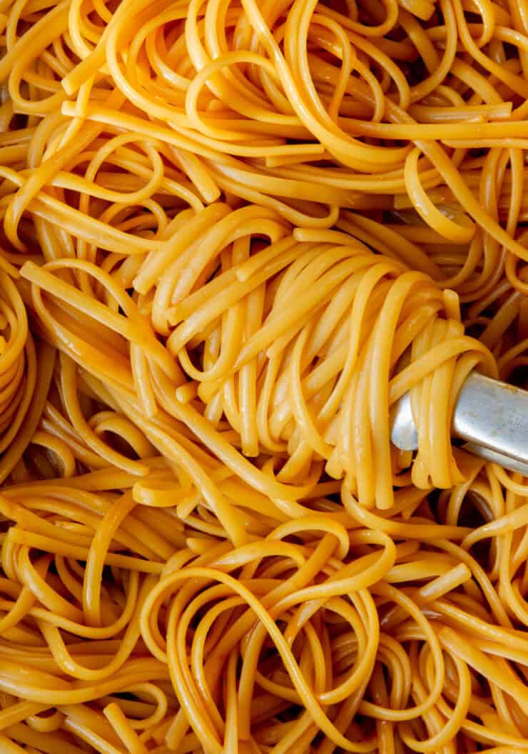 Close up of cooked spaghetti being stirred with some tongs with a sauce.