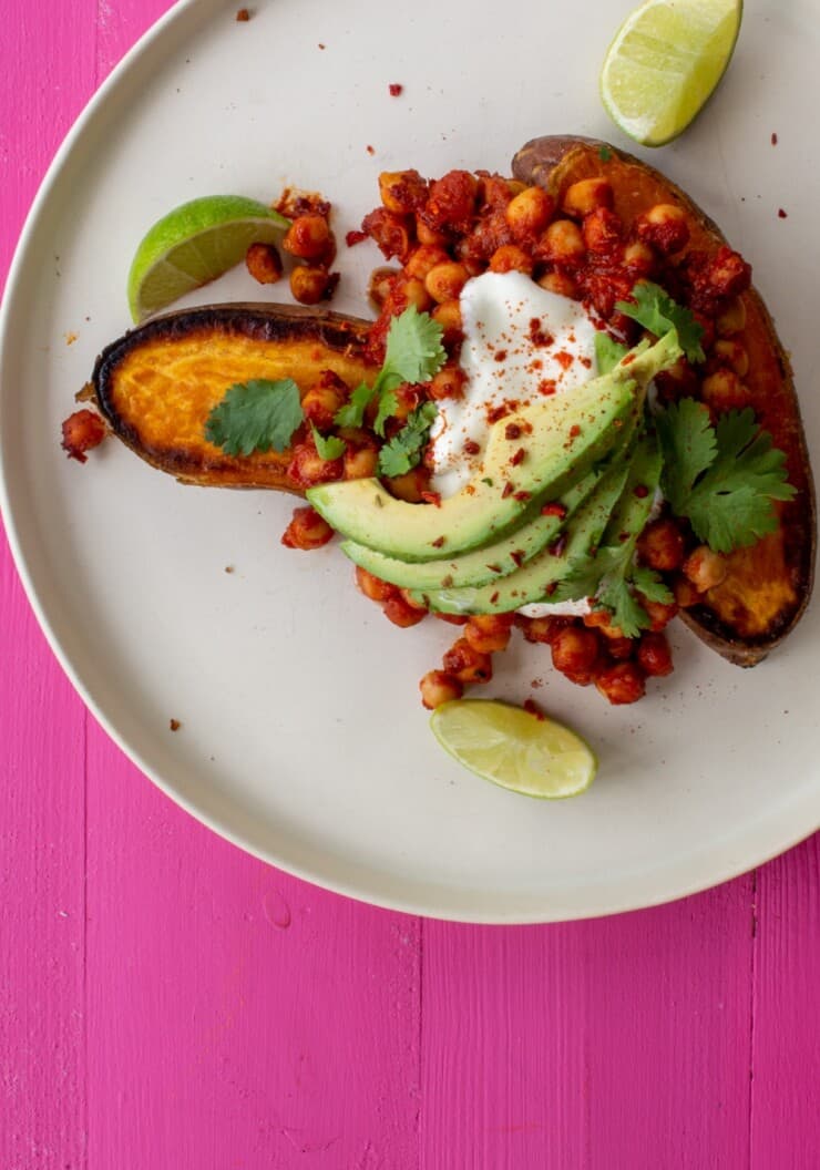 Spicy Chickpea and Roasted Sweet Potato Tray bake served on a plate and topped with avocado slices, sour cream and lime wedges.