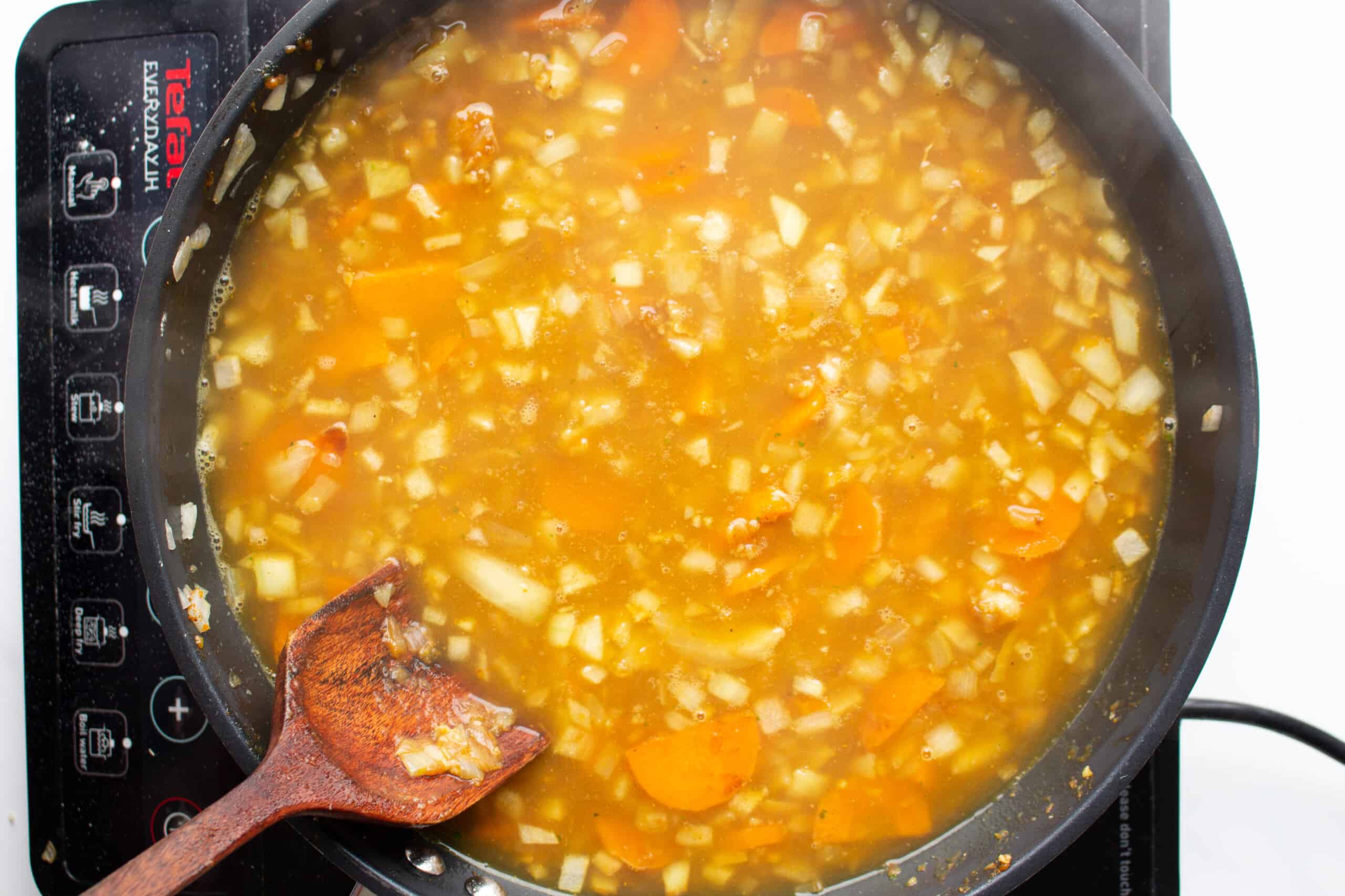 Carrots, onions and spices with chicken stock in pan