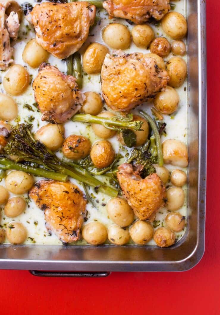 Creamy Lemon and Thyme Chicken Tray Bake with browned chicken thighs, broccoli stems and new potatoes in a creamy sauce on a baking tray.
