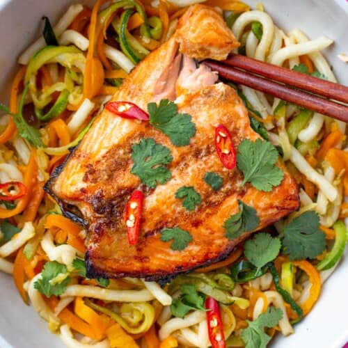 Salmon with chop sticks on a bed of noodles with spiralised courgettes and carrots topped with coriander and red chilli slices.