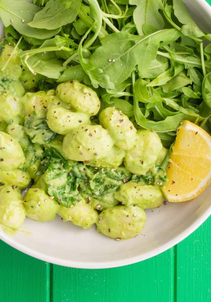 Overhead shot of bowl of green gnocchi with rocket salad and wedge of lime