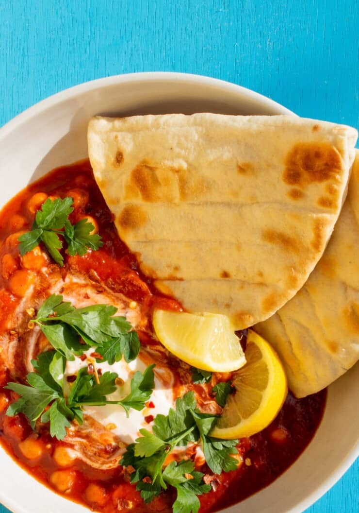 Overhead shot of harissa chickpea bowl with 2 flat bread halves and lemon wedges