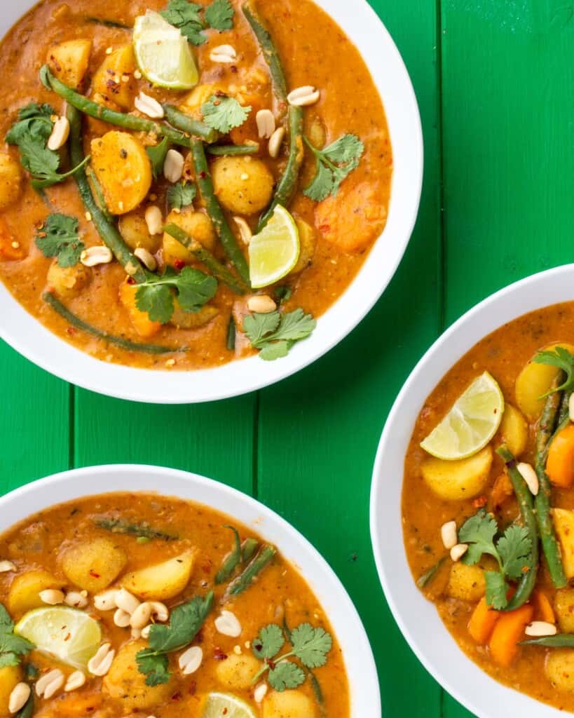3 white bowls of Massaman curry with new potatoes and vegetables and garnished with coriander.