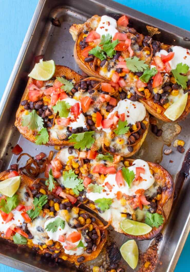 Overhead shot of 4 halves of butternut squash baked on tray topped with black beans, sour cream, tomatoes and garnishes