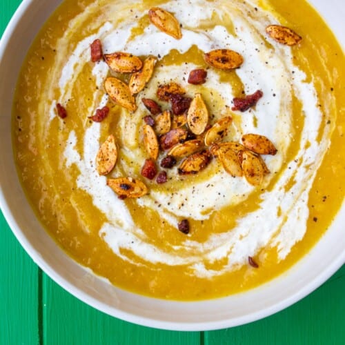 Over head shot of pumpkin soup in bowl and garnished with swirl of cream and toasted pumpkin seeds