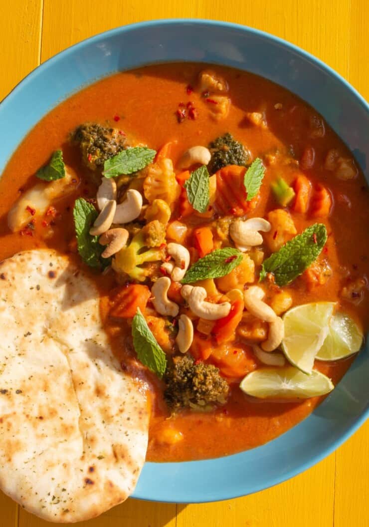 Overhead shot of bowl of vegetable curry with rice and naan bread