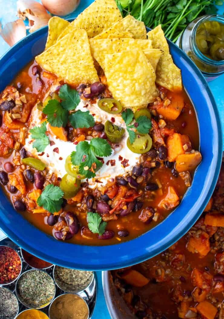 Overhead shot of sweet potato chilli con carne with tortilla chips, sour cream and coriander topping