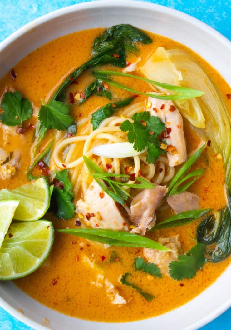 Creamy Spiced Thai Chicken Noodle Soup garnished with coriander, spring onion and lime wedges.