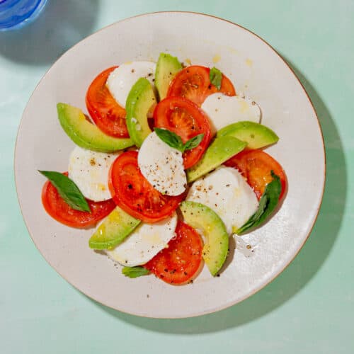 A bowl of salad with tomatoes, mozzarella and avocado in a decorated spiral on a white plate.