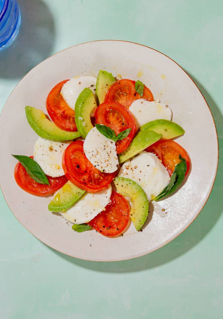 A bowl of salad with tomatoes, mozzarella and avocado in a decorated spiral on a white plate.