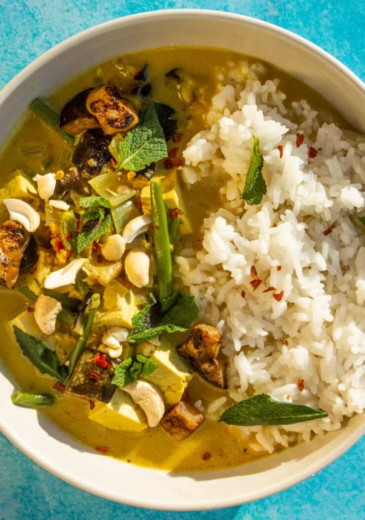 Overhead shot of bowl of tofu curry with rice and topped with cashews and mint