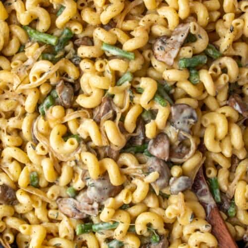 Close up of creamy mushroom stroganoff with spirali pasta with green beans with a wooden spoon.