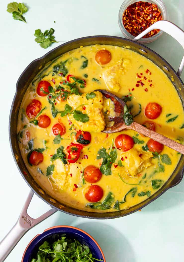 A large pan with yellowish curry with cherry tomatoes and coriander.