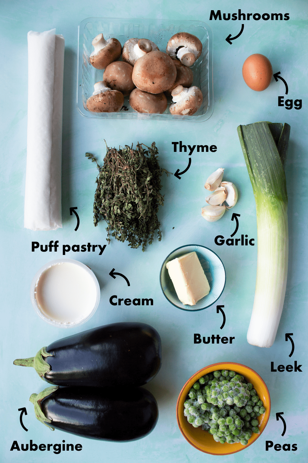 Ingredients to make Creamy Mushroom, Leek and Aubergine Vegetable Pie with Puff Pastry laid out on pale blue background and labelled.