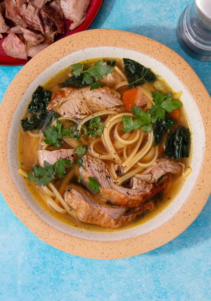 A bowl of turkey noodle soup with carrots, cavolo nero and parsley.